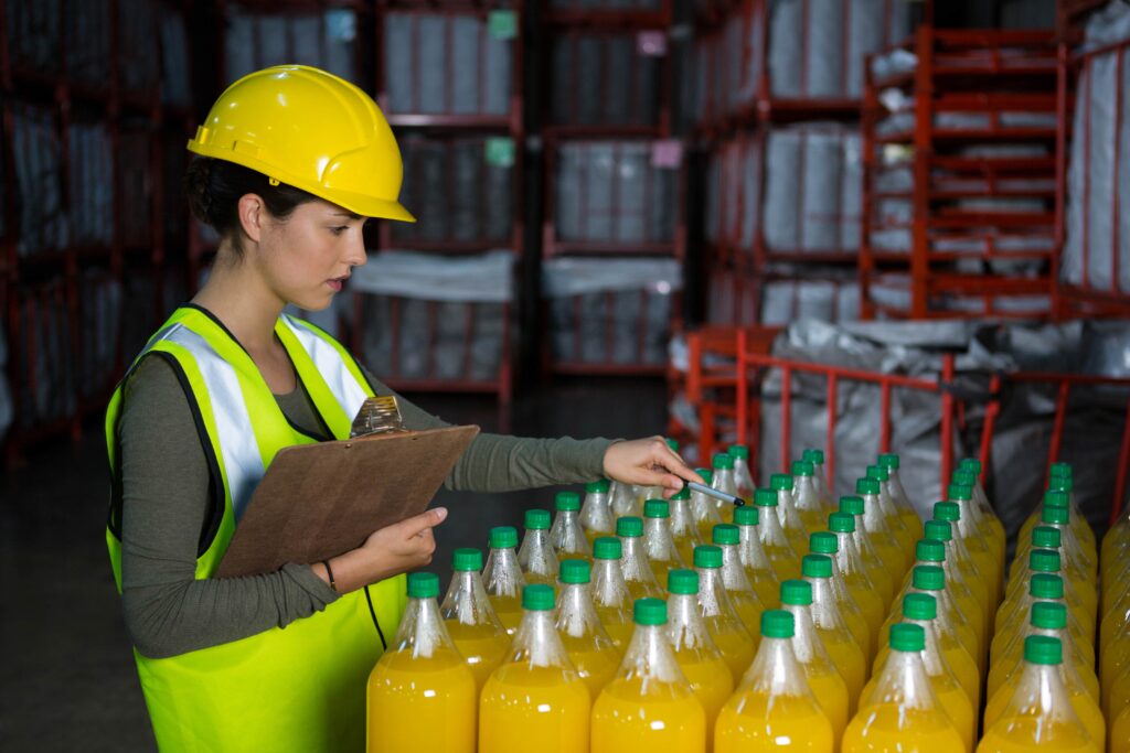 Factory worker in safety gear inspecting plastic bottles of juice in a warehouse