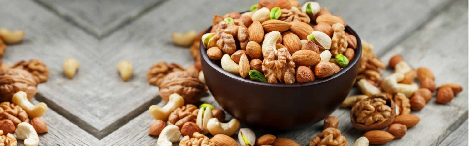 Assorted flavoured nuts including almonds, cashews and walnuts displayed in bowls for healthy snacking and premium gifting options.